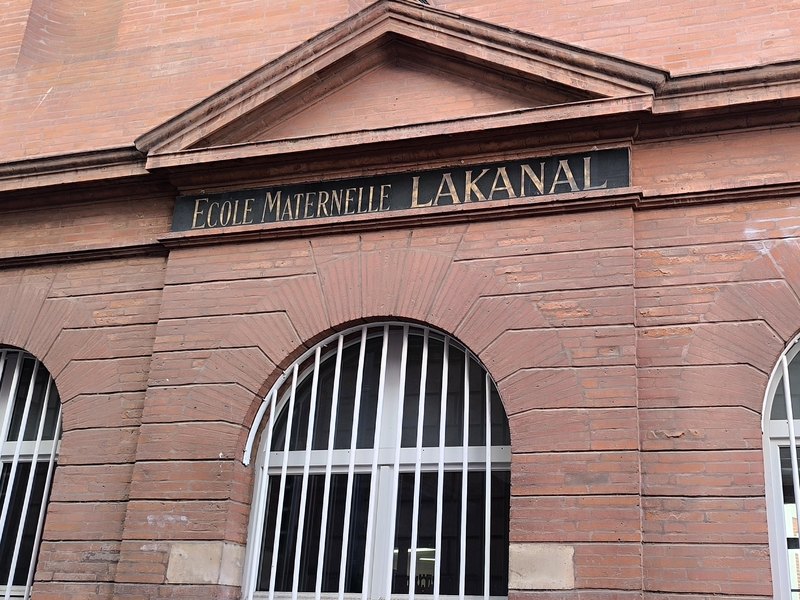 Façade en brique de l'école maternelle Lakanal, avec la plaque gravée portant son nom au-dessus des fenêtres en arc